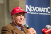 Niki Lauda mit roter Mütze und braunem Sakko spricht in ein Handmikrofon
